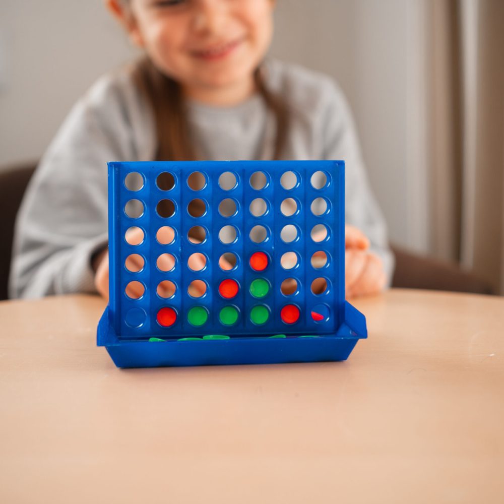 A child's focused smile behind a colorful board game, highlighting a moment of joy and strategy during playtime. High quality photo