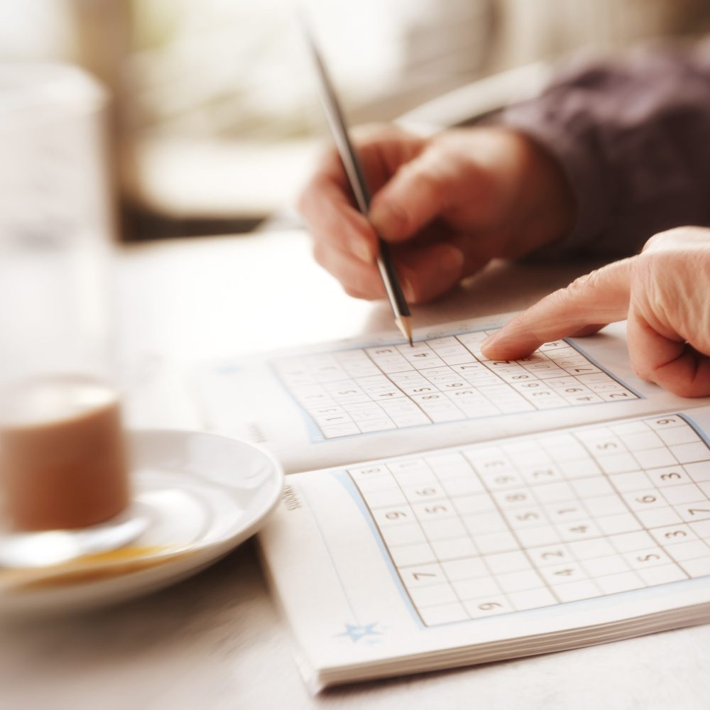 Woman trying to solve Sudoku Puzzle - window, sunlight, and coffee.